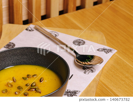 Warming pumpkin soup in bowl with seeds on wooden table Warming pumpkin soup in bowl with seeds on wooden table 140673782