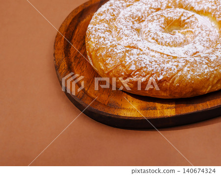 Ensaimada pastry with powdered sugar on wooden plate 140674324