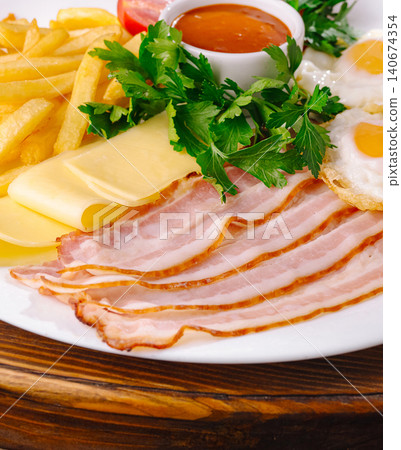 American breakfast plate featuring bacon, fried eggs, cheese, and french fries American breakfast plate featuring bacon, fried eggs, cheese, and french fries 140674354