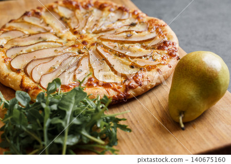 Pizza with pear and blue cheese, a bunch of young arugula, close-up of a delicious pizza and a concept of desserts and traditional baked goods Pizza with pear and blue cheese, a bunch of young arugula, close-up of a delicious pizza and a concept of desserts and traditional baked goods 140675160
