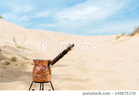 Brewing aromatic traditional coffee in a copper cezve on a sandy beach during siesta. Copy space for a text about coffee-making traditions Brewing aromatic traditional coffee in a copper cezve on a sandy beach during siesta. Copy space for a text about coffee-making traditions 140675170