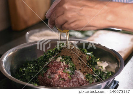Stirring eggs into ground meat and preparing the filling for dolma, hands of a chef preparing a traditional Georgian dish, close-up of the ground meat, spices, and herbs Stirring eggs into ground meat and preparing the filling for dolma, hands of a chef preparing a traditional Georgian dish, close-up of the ground meat, spices, and herbs 140675187