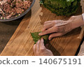 Woman's hands rolling grape leaves with stuffing, a top view of preparing dolma, a traditional Turkish and Mediterranean dish, copy space for text 140675191