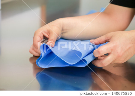 A dedicated medical professional carefully folds blue sterile surgical wrap on a stainless steel surface to maintain strict hygiene standards for a safe clinical procedure today A dedicated medical professional carefully folds blue sterile surgical wrap on a stainless steel surface to maintain strict hygiene standards for a safe clinical procedure today 140675850