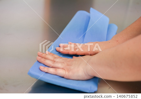 A medical professional carefully folds a sterile blue cloth on a stainless steel surface while preparing essential equipment for a surgical procedure to ensure patient safety today A medical professional carefully folds a sterile blue cloth on a stainless steel surface while preparing essential equipment for a surgical procedure to ensure patient safety today 140675852