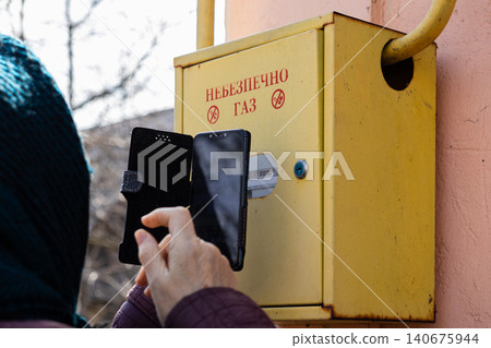 Person capturing an image of a yellow gas meter cabinet with a mobile phone, emphasizing the routine utility check process and the importance of monitoring household safety equipment Person capturing an image of a yellow gas meter cabinet with a mobile phone, emphasizing the routine utility check process and the importance of monitoring household safety equipment 140675944