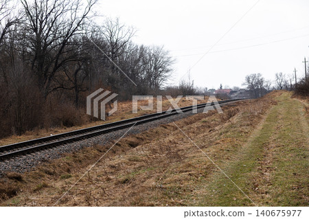 Railway tracks extending into the distance through a desolate rural landscape with bare autumn trees, creating a moody atmosphere of travel, transition and quiet solitude in nature Railway tracks extending into the distance through a desolate rural landscape with bare autumn trees, creating a moody atmosphere of travel, transition and quiet solitude in nature 140675977