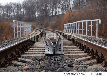 Railway track switch diverging into the distance on a bridge, capturing the industrial perspective and classic geometric lines of transportation infrastructure in autumn forests Railway track switch diverging into the distance on a bridge, capturing the industrial perspective and classic geometric lines of transportation infrastructure in autumn forests 140676006
