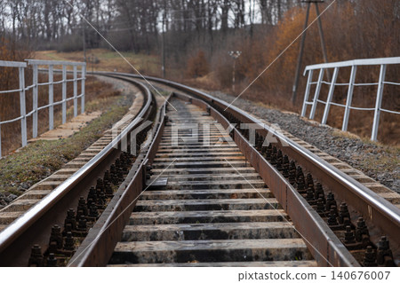 Railway tracks curve through a rural landscape with metal railings on a bridge, representing travel, transportation, and infrastructure development in a serene and moody setting Railway tracks curve through a rural landscape with metal railings on a bridge, representing travel, transportation, and infrastructure development in a serene and moody setting 140676007