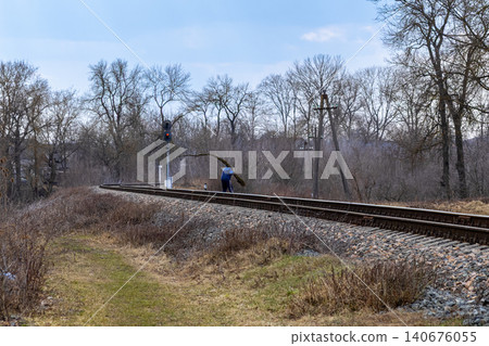 Person carrying a large fallen tree branch across rural railway tracks in a desolate landscape, illustrating a sense of struggle or hard work within a quiet natural winter setting 140676055
