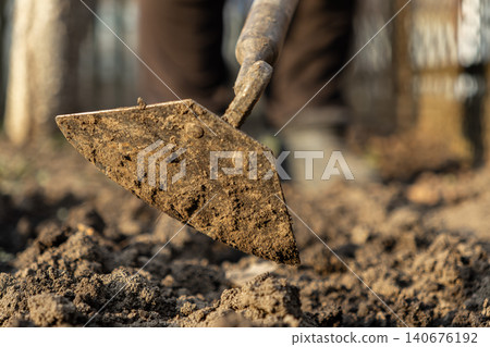 Metal hoe breaking up soil in a vegetable garden, showcasing professional agricultural labor and the preparation of earth for planting crops during a productive sunny spring season 140676192