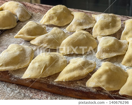 Raw handmade dumplings arranged on a floured wooden cutting board, capturing the authentic process of preparing traditional dough filled parcels for a delicious homemade meal project 140676296