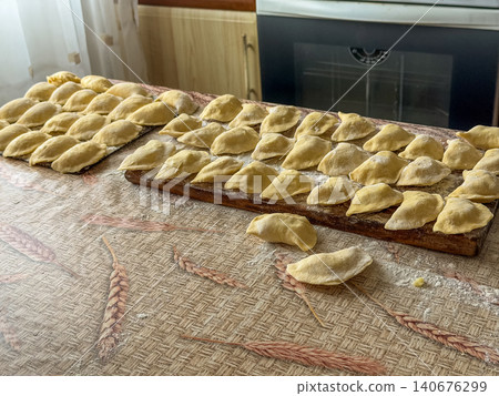 Fresh handmade dumplings arranged on wooden boards in a sunlit kitchen, representing traditional home cooking preparation and authentic culinary skills for a delicious family meal time 140676299