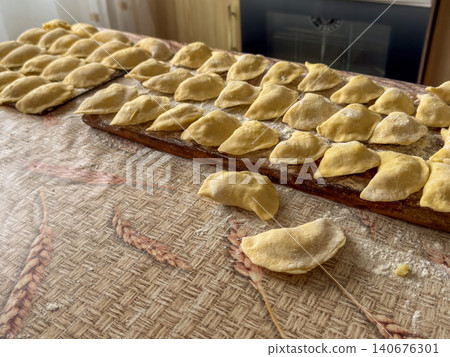 Fresh handmade dumplings arranged on a wooden board across a kitchen table, capturing the traditional process of preparing authentic homemade dough food for a rustic meal experience 140676301