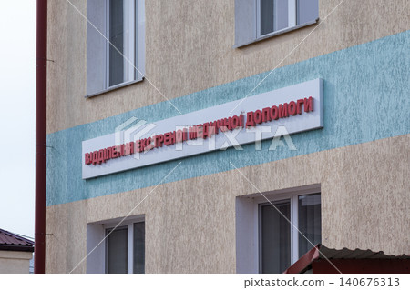 A red signage on a beige hospital wall indicating an emergency medical department entrance, establishing clear navigation for urgent healthcare access in a modern urban clinic building A red signage on a beige hospital wall indicating an emergency medical department entrance, establishing clear navigation for urgent healthcare access in a modern urban clinic building 140676313