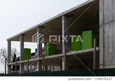 Unfinished concrete building frame with bright green insulation blocks on the open floor levels, representing modern urban construction progress and architectural development industry Unfinished concrete building frame with bright green insulation blocks on the open floor levels, representing modern urban construction progress and architectural development industry 140676327