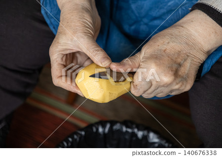 Elderly hands carefully peel a fresh potato with a small knife, highlighting traditional food preparation and domestic kitchen skills in a peaceful home setting during daily cooking Elderly hands carefully peel a fresh potato with a small knife, highlighting traditional food preparation and domestic kitchen skills in a peaceful home setting during daily cooking 140676338