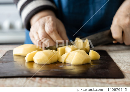 A senior person carefully cuts a raw peeled potato on a dark kitchen board, illustrating culinary preparation and healthy homemade cooking techniques for delicious nutritious meals A senior person carefully cuts a raw peeled potato on a dark kitchen board, illustrating culinary preparation and healthy homemade cooking techniques for delicious nutritious meals 140676345
