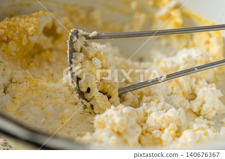 Cottage cheese being mashed with a metal tool in a bowl to create a smooth texture, capturing a practical cooking preparation process for a healthy homemade meal or dairy snack Cottage cheese being mashed with a metal tool in a bowl to create a smooth texture, capturing a practical cooking preparation process for a healthy homemade meal or dairy snack 140676367