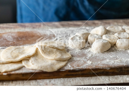 Fresh dough balls and rolled flat discs sitting on a floured wooden board, representing traditional dumpling preparation in a rustic kitchen setting focused on homemade meal cooking 140676404