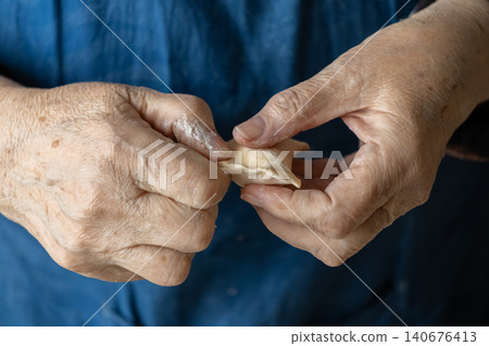 An elderly person carefully shapes a fresh handmade dumpling with floured hands, representing traditional culinary craftsmanship, wholesome home cooking, and authentic heritage food An elderly person carefully shapes a fresh handmade dumpling with floured hands, representing traditional culinary craftsmanship, wholesome home cooking, and authentic heritage food 140676413