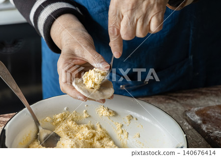 A senior person fills small dough circles with fresh cheese to prepare handmade dumplings, emphasizing the traditional culinary process in a cozy home kitchen cooking environment setup 140676414