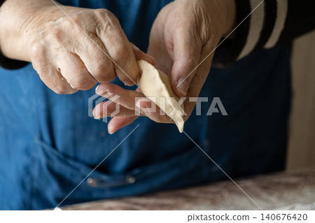 Elderly person pinching edges of a fresh raw dumpling dough piece by hand, capturing a traditional culinary technique for making authentic homemade food in a cozy kitchen setting Elderly person pinching edges of a fresh raw dumpling dough piece by hand, capturing a traditional culinary technique for making authentic homemade food in a cozy kitchen setting 140676420