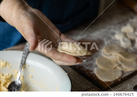 A hand shaping a fresh homemade dumpling over a rustic kitchen table, capturing the traditional craft of preparing authentic handmade dough food in a warm home culinary atmosphere A hand shaping a fresh homemade dumpling over a rustic kitchen table, capturing the traditional craft of preparing authentic handmade dough food in a warm home culinary atmosphere 140676425