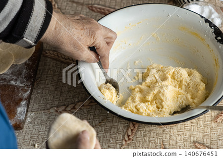 A senior person fills raw dough for homemade dumplings using a spoon in a rustic kitchen setting, capturing the traditional process of creating authentic food with fresh ingredients A senior person fills raw dough for homemade dumplings using a spoon in a rustic kitchen setting, capturing the traditional process of creating authentic food with fresh ingredients 140676451