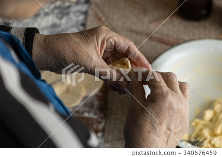 A senior person carefully shaping homemade dumplings by hand in a rustic kitchen, conveying culinary heritage and traditional cooking skills through the precise movement of aged fingers A senior person carefully shaping homemade dumplings by hand in a rustic kitchen, conveying culinary heritage and traditional cooking skills through the precise movement of aged fingers 140676459