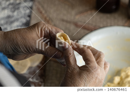 A senior person folds homemade dough with cottage cheese filling to create delicious dumplings, capturing the traditional craft of artisanal cooking within a rustic warm home kitchen A senior person folds homemade dough with cottage cheese filling to create delicious dumplings, capturing the traditional craft of artisanal cooking within a rustic warm home kitchen 140676461