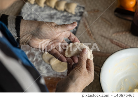 An elderly person shaping handmade dumplings by hand on a rustic table, highlighting traditional culinary skills and the warmth of preparing authentic homemade food in a cozy kitchen An elderly person shaping handmade dumplings by hand on a rustic table, highlighting traditional culinary skills and the warmth of preparing authentic homemade food in a cozy kitchen 140676465