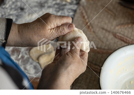 A senior person carefully shaping handmade dumplings on a floury surface, highlighting the tradition of craft and the warmth of preparing a wholesome meal within a rustic home kitchen A senior person carefully shaping handmade dumplings on a floury surface, highlighting the tradition of craft and the warmth of preparing a wholesome meal within a rustic home kitchen 140676466