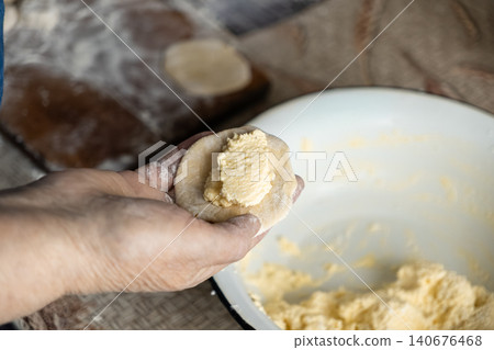 A hand holds a fresh dumpling dough round filled with creamy cheese to illustrate the artisanal preparation of homemade pastry dishes in a rustic kitchen setting during meal cooking A hand holds a fresh dumpling dough round filled with creamy cheese to illustrate the artisanal preparation of homemade pastry dishes in a rustic kitchen setting during meal cooking 140676468