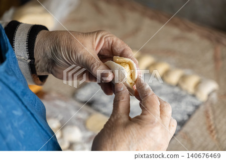 A senior person carefully shaping homemade dumplings by hand on a dusted kitchen table, highlighting traditional culinary skills and the authentic craft of preparing fresh food meals A senior person carefully shaping homemade dumplings by hand on a dusted kitchen table, highlighting traditional culinary skills and the authentic craft of preparing fresh food meals 140676469