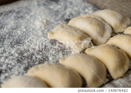 Fresh handmade dumplings arranged on a rustic wooden board dusted with wheat flour, reflecting authentic culinary preparation for traditional homemade cooking and healthy meal recipes 140676482
