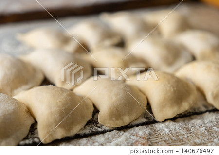 Fresh handmade dumplings arranged on a wooden board covered with white flour, showcasing culinary preparation steps for traditional comfort food in a rustic home kitchen environment 140676497