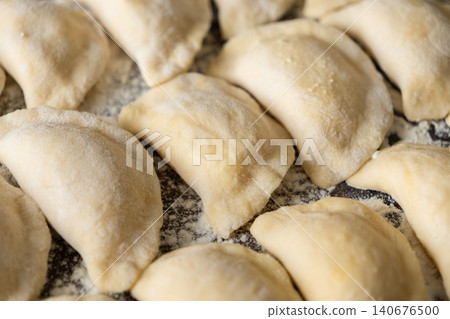 Fresh handmade dumplings arranged on a floured surface, capturing the traditional preparation process for hearty meals in a cozy home kitchen setting focused on artisan culinary work Fresh handmade dumplings arranged on a floured surface, capturing the traditional preparation process for hearty meals in a cozy home kitchen setting focused on artisan culinary work 140676500