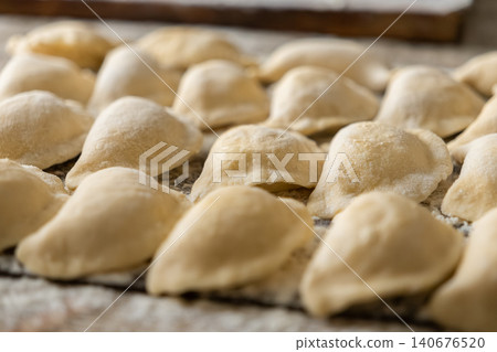 Fresh homemade raw dumplings resting on a floured wooden surface before cooking to illustrate culinary preparation for traditional rustic cuisine in a warm domestic kitchen setting Fresh homemade raw dumplings resting on a floured wooden surface before cooking to illustrate culinary preparation for traditional rustic cuisine in a warm domestic kitchen setting 140676520