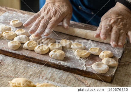 Senior hands prepare handmade dough pieces on a wooden cutting board to shape fresh dumplings, capturing traditional culinary skills and the authentic warmth of home cooking heritage Senior hands prepare handmade dough pieces on a wooden cutting board to shape fresh dumplings, capturing traditional culinary skills and the authentic warmth of home cooking heritage 140676530