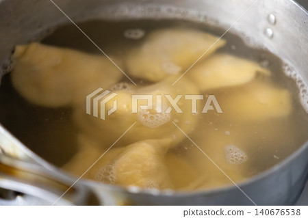 A metal pot full of boiling water with several savory dumplings inside, highlighting the process of cooking traditional food and the preparation of a homemade meal for hungry guests A metal pot full of boiling water with several savory dumplings inside, highlighting the process of cooking traditional food and the preparation of a homemade meal for hungry guests 140676538
