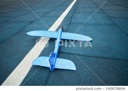 Wide urban court view with plane on surface, blue speckled glider resting on rubber tiles, apartment blocks and street visible in background, community 140676604