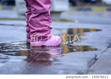 Toddler in pink waterproof suit and boots walking through puddles in spring park Toddler in pink waterproof suit and boots walking through puddles in spring park 140676611