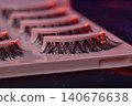 Macro eyelash trays under purple light, lash artist prep station showcasing strip lashes on glossy white trays, neon lighting casting pink highlights, shallow depth 140676638