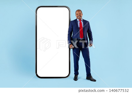 Mature black businessman in suit holding folder, standing beside giant blank smartphone Mature black businessman in suit holding folder, standing beside giant blank smartphone 140677532