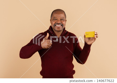Smiling mature black man holding yellow credit card and showing thumbs up Smiling mature black man holding yellow credit card and showing thumbs up 140677622