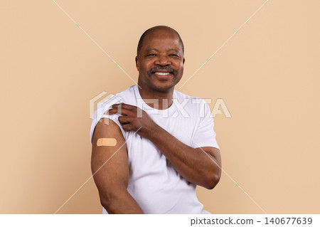 Mature black man in white shirt showing bandage on arm after vaccination Mature black man in white shirt showing bandage on arm after vaccination 140677639