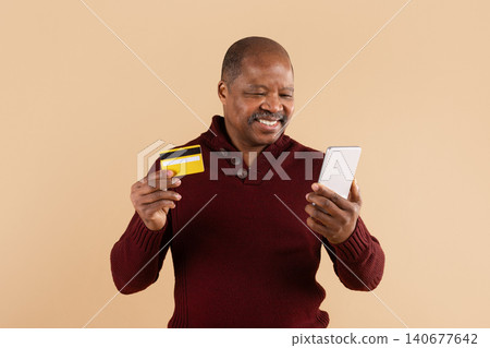 Mature African American man smiling while holding smartphone and credit card 140677642