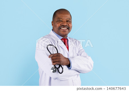 Smiling mature black doctor in white coat holding stethoscope with arms crossed 140677643