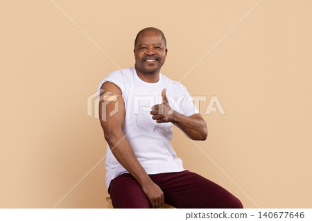 Mature African American man showing vaccination bandage on arm with thumbs up Mature African American man showing vaccination bandage on arm with thumbs up 140677646